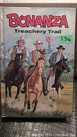 Front cover of vintage Bonanza Treachery Trail western book showing three cowboys riding horses with mountain background.
