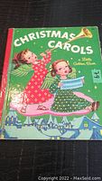 Front cover of the vintage Christmas Carols book showing two angels with musical notes and a green background.
