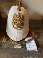 Full frontal view of helmet on table showing white canvas cover, brass crest and chain chin strap.