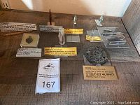 Overview of six artifacts on wooden shelf: belt buckle, arrowheads, spear point, shield plate with labels