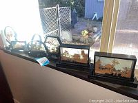 Set of six Asian decorative carvings in glass shadow boxes displayed on a window ledge, showing different intricate scenes and frame shapes.