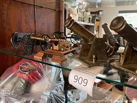 Three miniature cannon replicas displayed on glass shelf, two on angled cast iron bases and one on wooden plinth