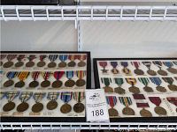 Four black wood frames on white wall shelf containing rows of metal service medals on colored ribbons.