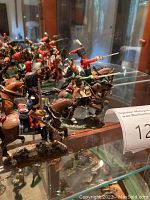Group of painted metal cavalry soldier figurines and horses on glass shelf