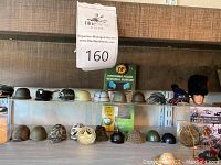 Two-tier shelf displaying fourteen miniature helmets, caps and wooden-handled paddle sign
