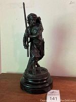 Front view of the dark patina heavy metal soldier sculpture holding a long gun, standing on a wooden base.