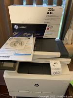 Front view of laser printer with HP 202X black toner box, HP 202A magenta toner box and user manuals on top