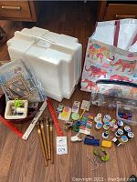 Full lot overview showing sewing machine case, tote bag, quilt patterns, thread spools, tools including scissors and clips, and wooden spools laid out on floor.