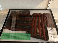 Framed display case showing two sections of Japanese samurai armor plates with green informational label