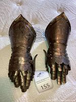 Pair of steel gauntlets displayed side by side on fabric background, wall-mount brackets visible