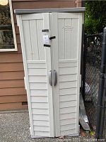 Front closed view of beige plastic outdoor storage shed with double doors and Suncast brand logo visible.