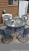 Round glass-top patio table with black metal frame surrounded by four swivel chairs