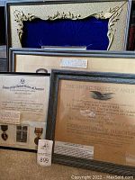 Three framed items grouped on floor: ornate gilt frame with blue velvet backing at top, two silver-tone frames below