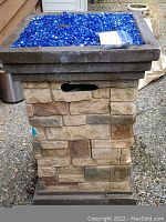 Front view of fire pit table filled with blue glass stones and faux stone pedestal