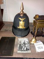Overview of spiked helmet, glass plate, postcard, brass vessel and brass helmet figurine