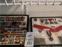 Two framed displays of various medals, pins and a banknote on a shelf