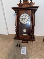 Full front view of clock case with two loose turned finials and lot tag.