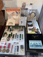 Multiple WW2 service medals on display board alongside Rosie the Riveter sheet music, posters, newspaper clippings and other ephemera.