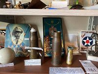 Overview of ceramic grenade, shell casings, brass cartridge, officer tin and South Pacific plaque on shelf