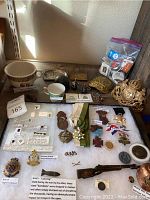 Overall lot on shelf showing cups, inkwell, decorative brass pieces, bag of pennies, small medals and badges on board