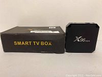 Black X96mini Smart TV Box placed next to its original black packaging labeled "SMART TV BOX" in yellow text.