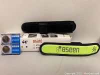 Two BSeen arm bands (one yellow-green with logo and one black) placed on top of a white BSafe box along with a pack of two CR2032 batteries.