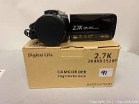 Camcorder on its cardboard box with front side visible showing the lens and printed specs.