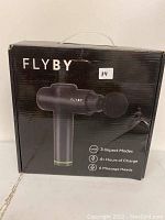 Closed box showing FLYBY massage gun, listing 3 impact modes, 4+ hours charge, 6 massage heads