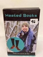 Box front view showing heated socks designed to keep warm all day, featuring a winter-themed image and graphic representation of heating elements in the socks.