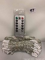 Coiled LED string lights bundled with a clear wire and an accompanying remote control with multiple buttons visible.