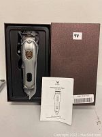 Image of silver Misiki hair trimmer in black plastic tray, with user manual and brown textured box alongside.