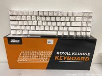 Photo showing the white compact Royal Kludge keyboard on top of its original black and orange box.