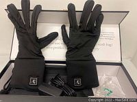 Pair of black Savior heated gloves displayed palm-side up inside a box with included charging adapter and cable.