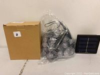 Photo of solar panel, bundled string lights in clear plastic, and a plain cardboard box.