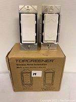 Two TopGreener in-wall dimmer switches resting on their retail packaging box. One switch is a single paddle style, the other has up and down arrow paddles. The box indicates the product is a Wi-Fi wireless dimmer 3 way kit.