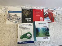 Photo showing seven assorted engineering textbooks including Operating Systems in Depth, Research Design, Mechanics of Materials, Eaton manual, Autodesk Inventor 2016, Circuit Analysis.
