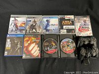 Photo showing the 2 PlayStation 2 controllers and 9 PlayStation games including The Last of Us on PS4 and NHL 2k6 on PS2 arranged on black surface