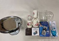Photo showing LED makeup mirror, packaged shower razor, battery pack, a clear glass cup, and ceramic bathroom accessories with floral design.