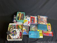 Large assortment of children's arts and crafts supplies including colored pencils, crayons, watercolor paint palettes, glue sticks, and paint palette on a black background.