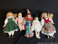 Photo of the collection of 5 dolls arranged side by side on a black background, showing size and details of clothing and faces