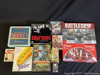 Photo of the full collection of 11 games showing the boxes and tins including Sorry, The Sopranos Trivia Game, Battleship, Chess, and several card games.