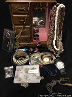 Jewellery box with drawers open surrounded by assorted jewellery including watches, bracelets, necklaces, and earrings.