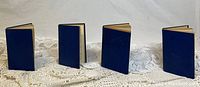 Four hardcover books with blue covers standing upright on a white lace cloth.