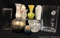 Front view of assortment of vases arranged on black surface including glass, brass, ceramic, and crystal types with various patterns and colors.