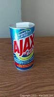 Front view of the fake Ajax bleach powder container showing branding and product name in red and white text on a blue canister.