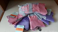 Top-down view of all 5 gloves showing 2 pairs purple and 3 pairs pink, new with tags attached.