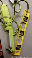 Yellow handheld hanging light with plug-in socket and power cord, next to a yellow spirit level with bubble vials and handle cutout.