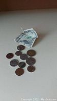 One US one-dollar bill and eleven assorted coins on a flat surface, showing various coin sizes and designs.