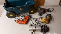 Four corded power tools on a flat surface next to a green plastic container with yellow wheels