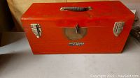 Photo of red metal toolbox closed with front view showing latches and handle.